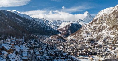 Zermatt, İsviçre 'nin havadan görünüşü, sağda Matterhorn, dağ evi çatıları, lüks oteller, dolambaçlı sokaklar, donmuş bir spor alanı, ve açık gün ortası aydınlığı..