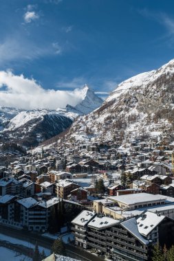 İsviçre, Zermatt 'ın havadan görünüşü, Matterhorn, karla kaplı çatılar, dağ evi otelleri, ve aydınlık kış güneşi altında kilise kulesi, etrafındaki bulutlar.