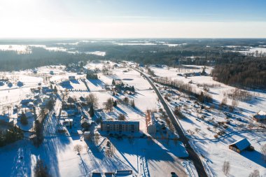 Sigulda ve Turaida yakınlarındaki hava sahnesinde karlı tarlalar, köy evleri, çiftlik evleri ve uzun mavi gölgelerle karanlık ormanlık tepelere uzanan dolambaçlı bir yol görülüyor..