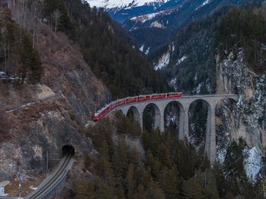 Gökyüzü görüntüsü Graubunden, İsviçre 'deki Landwasser Viaduct' ı gösteriyor. Kızıl Buzul Ekspresi öğleden sonra saatlerinde bir uçurum tüneline doğru altı kemer üzerinde kıvrılıyor..