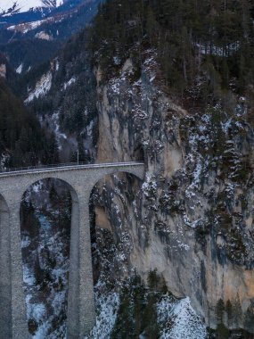 Taştan kemerler Graubunden, İsviçre 'deki bir nehrin yukarısındaki uçurum tüneline doğru kıvrılır. Serin mavi tonlar ve dağınık kar kışın başlarında ve öğleden sonra güneşinin altında.
