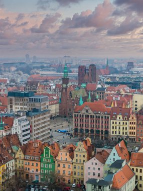 Hava görüntüsü Wroclaw Eski Kasabası Rynek ve Gotik Belediye Binası 'nın alacakaranlıkta olduğunu gösteriyor. Tramvaylar ve insanlar aşağı hareket eder, pastel cepheler meydanı kuşatır, katedral kuleleri sis içinde yükselir..