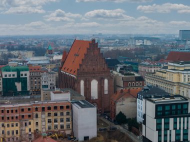 Polonya 'nın merkezindeki Wroclaw şehrinin hava manzarası, Aziz Mary Magdalene Kilisesi' nin tuğlasını gösteriyor. Pastel cephelerin ve yumuşak gün ışığı altında cam ofislerin ve bulutların arasında..