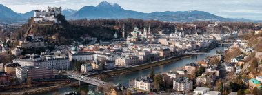 Avusturya 'nın Salzburg kentinin havadan görünüşü, Hohensalzburg Kalesi' nin ormanlık bir tepe, Salzburg Katedrali kubbeleri, Salzach Nehri üzerindeki köprüler ve yumuşak kış günışığı altındaki Alpler..