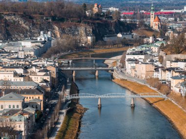 Avusturya 'nın Salzburg kentinin hava manzarası Salzach Nehri' ni Makartsteg ve karayolu köprüleri, yeşil kulesi olan bir kilise, Monchsberg, çıplak ağaçlar ve yumuşak kış ışığı ile gösteriyor..