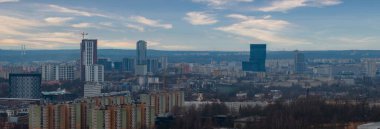 Polonya, Katowice 'nin geniş hava manzarasında sosyalist dönem blokları, KTW mavi cam kuleler, yüksek binalar ve turnalar serin gün ışığında ağaçlık tepeler ve çizgili bulutlar görülüyor..