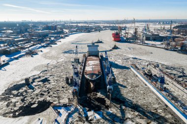 Riga Tersanesi 'nin hava sahnesine göre, yüzen bir rıhtımda bir gemi, kırık nehir buzu, kanat vinçleri, ve iskele vinçleri, Daugava Nehri' nde kırmızı bir gemi ve römorkör izleri var..