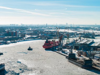 Riga, Letonya 'daki Riga Tersanesi' nin hava görüntülerine göre donmuş Daugava Nehri 'nde vinçler, kuru rıhtımlar, römorkörler ve kırmızı bir gemi var. Kar, solgun bir gökyüzünün altında parlak bir ışığı yansıtır..