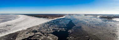Donmuş Daugava 'nın Riga, Letonya' da Baltık Denizi 'yle buluşmasını gösteren hava manzarası. Buz kütleleri, karlı dalgalar, Mangalsala deniz feneri ve Riga Tersanesi vinçleri..