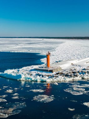 Hava sahnesinde Mangalsala Deniz feneri Riga, Letonya 'da buzlu bir dalgakıranda görünüyor. Koyu mavi Daugava donmuş Baltık 'la karşılaşıyor, yüzüyor ve parlak gün ışığında buzdan bir kanal açılıyor..