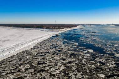 Hava görüntüsü Letonya, Riga yakınlarındaki Daugava Nehri ağzında kayan gözleme buz kütlelerini gösteriyor. Mangalsala kum tepeleri, Mangalsala Deniz feneri ve Riga Tersanesi vinçleri gün ışığında..