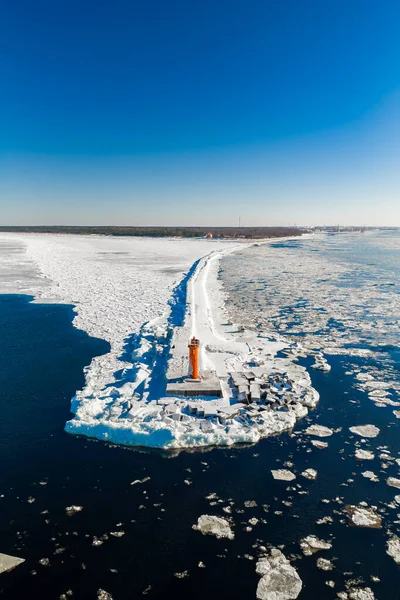 Hava görüntüsü, Daugava Nehri 'nin Riga' da Baltık Denizi 'yle birleştiği yerde, ufukta liman yapıları olan parlak turuncu Mangalsala Deniz Feneri' ni gösteriyor..