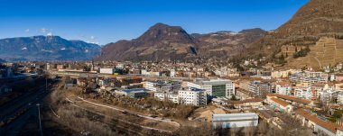 Bolzano, İtalya 'da geniş bir hava manzarası, Monte Tondo' yu, teraslı üzüm bağlarını, bir tren istasyonunu, pastel blokları, ofisleri ve kışın hafif ışığı altında bir kilise kulesini ve açık gökyüzünü gösteriyor..