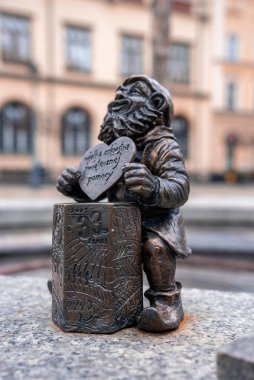 Küçük bir bronz cüce kalp plaketi taşıyor ve Polonya 'nın Wroclaw kentindeki 2025 kutusuna yaslanıyor. Bulanık tarihi konutlar, yumuşak gün ışığı ve sığ alan derinliği..