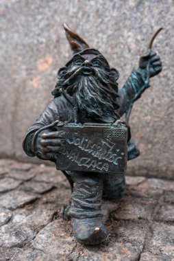 Wroclaw, Polonya, bronz cüce kaldırım taşlarının üzerine diz çöker, Solidarnosc Walczaca yazılı bir levha tutar ve eğri büğrü bir nesne, parlak ayak parmağı görünür, sığ alan derinliği.