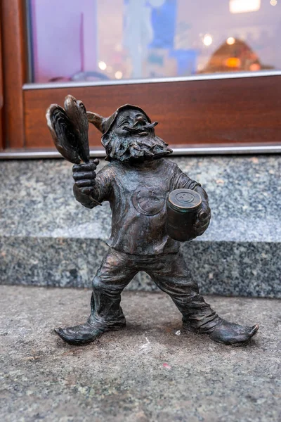 Bronz Wroclaw krasnal granit bir çıkıntının üzerinde duruyor, şehir merkezindeki bir dükkanın önünde teneke ve tava tutuyor, açık havada, gün ışığında..