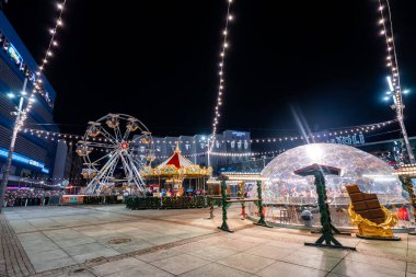Orta Katowice, Polonya 'da gece panayırı, sicim ışıkları, küçük bir dönme dolap, klasik bir atlıkarınca, bir igloo barı, altın bir kızak, Aparthotel ve Aioli işaretleri..