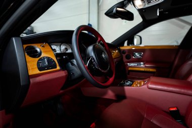 Rolls Royce Phantom 'un dahili görüntüsünde burgonya derisi, cilalanmış ahşap, krom, RR amblem tekerleği, beyaz analog göstergeler ve yumuşak ışık altında knurled kontroller görülüyor..