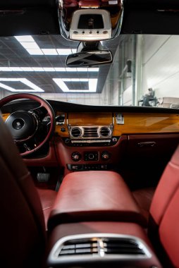 Arka koltuklardan Rolls Royce Phantom kokpitinin yakın görüntüsü, RR direksiyon simidi, parlak tahta torpido, krom kapaklar, koyu kırmızı deri ve parlak tavan ışıkları..