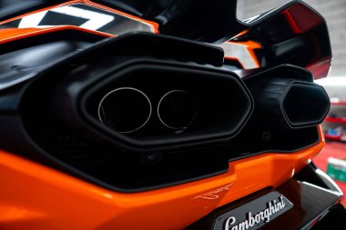 Altıgen çevrede ikiz merkezi egzoz uçları Lamborghini senaryosunun üstündeki havalandırma ve karbon süslemesi arasında oturur. Araçlar ve raflar dramatik ışık gibi yumuşak görünür..