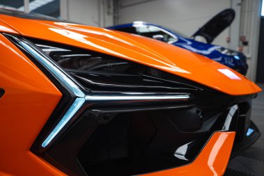 Lamborghini Revuelto 'nun far ışığı, Y şeklindeki LED ışıklar, çokgen kaporta, ve bir atölyede karbon fiber kanal, açık bir kaputun altında mavi bir araba..