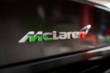 Sığ bir alan derinliği krom McLaren rozeti çerçeveler Bir otomotiv atölyesinde parlak siyah panel üzerinde, hız işareti kırmızı n ve yumuşak bokeh yakın.