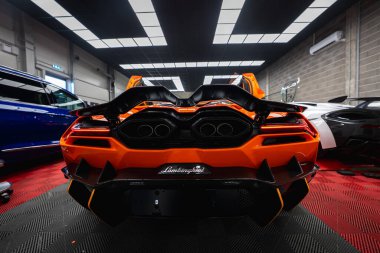 Turuncu Lamborghini Revuelto kapalı bir akort bölümünde oturur, kuad egzozları merkezi, siyah aero yüzgeçleri ve dağıtıcı, Lamborghini betiği görünür, teftiş ayarları.