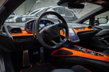 Lamborghini Revuelto 'nun sihirli direksiyonlu, Revuelto grafikli, merkezi dokunmatik ekran, turuncu aksanlı, karbon fiber süslemeli ve görünür metal pedallı kapalı galeri kokpiti..