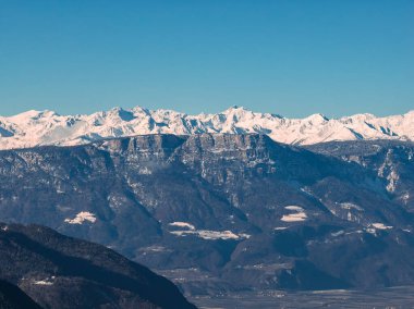Kuzey İtalya 'daki geniş bir vadinin üzerinde engebeli orman tepeleri ve tırtıklı kireçtaşı kayalıkları yükseliyor. Karla kaplı zirveler kıtır ışık altında, çiftlikler ve teraslar aşağıda..