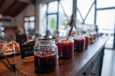 Bir Dolomitler butik otelinde, üzerinde kaşık ve etiketler bulunan cam kavanozlar dolusu ev yapımı reçeller. Sabah ışığı ve sığ alan derinliği arkasında bulanık hamur işleri.