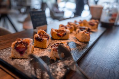 Isırık büyüklüğünde erikli kek kareleri pudra şekeriyle tozlanmış maşayla tahtaya oturuyorlar. Kırsal masa, karatahta tabelaları ve oturma odaları Dolomitler 'in kafe düzenini öneriyor..