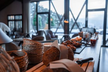 Tohumlu somunlar, kruvasanlar, reçeller ve hasır sepetler uzun bir masada oturur. Yerden tavana pencereler çerçeveli, karlı, yemyeşil ve kış sabahı uzak dağlar..