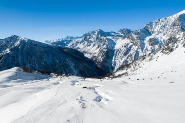 İtalyan Alpleri 'ndeki San Domenico' nun havadan görünüşü, bakımlı koşular, kayakçılar, asansörler, pansiyonlar, sivri tepeler, derin bir vadi ve dağın ortasındaki geniş toz alanları gösteriyor..