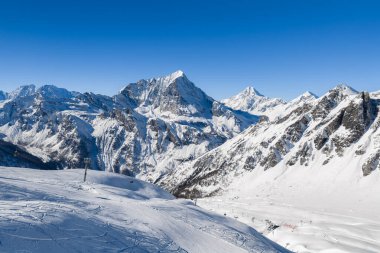 İtalyan Alpleri 'ndeki San Domenico kayak merkezinin hava manzarasına göre geniş kar yamaçlarında raylar, asansör sütunları, engebeli tepeler, tepeler, tepeler ve kayakçılar var..
