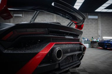 Arka planda Huracan rozeti, ikiz egzozlar, açısal dağıtıcı ve yükseltilmiş kanat var. Kırmızı süslemeli mat siyah, karbon fiber, panel aydınlatma, raflar ve bulanık bir spor araba..