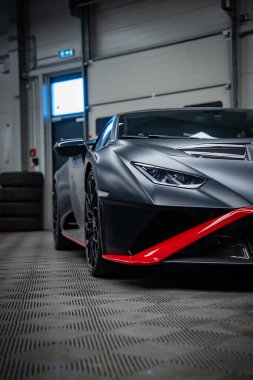 Ön tarafı kapayın. Siyah Lamborghini Huracan atölyesinde, Y şeklinde LED farlar, kırmızı kırbaç ve süsleme, yer döşemeleri, lastikler ve garaj kapısı..