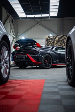 Bir mat siyah Lamborghini Huracan modern bir garajda oturuyor, arka alçak açı manzaralı, motor kapağı açık, kırmızı aero aksanlı, sabit kanatlı, çift merkezli egzozlar, tekerlek çerçeveli sahne.