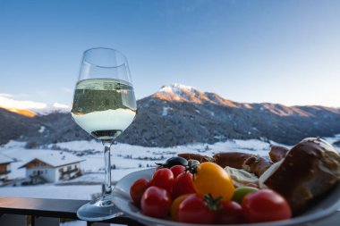 Otel balkon masasında beyaz şarap, domates, zeytin, peynir ve ekmek var. Günışığı Dolomitleri kış mevsiminde kuzey İtalya 'da Alp Vadisi' nde karla kaplı bir vadide yükselirler..
