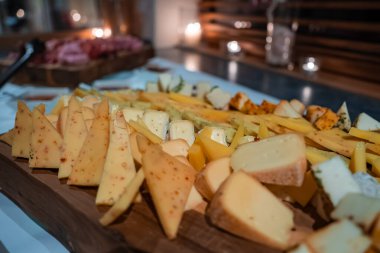Peynir tahtasını kırsal bir zemine kapatınca Alp kamaları, kremsi maviler ve yumuşak kabuklular görünüyor. Sıcak mum ışığı, ahşap ve metal döşeme, gece ayarı, sığ alan derinliği..