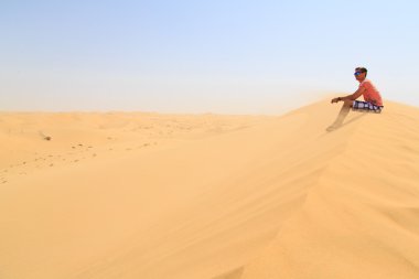 Bir çölde bir kumul üzerinde oturan genç adam