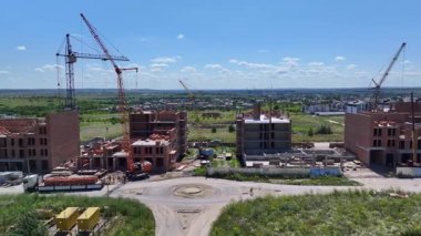 Construction site with cranes and unfinished brick buildings, modern housing project development in progress under clear blue sky.