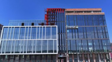 Modern glass office building under construction with clear blue sky, reflecting windows and workers on suspended platform, urban architecture project in progress.