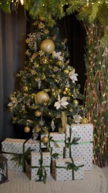 Altın süslemelerle süslenmiş zarif Noel ağacı ve ışıl ışıl parıldayan ışıklar, güzelce paketlenmiş hediyelerle ayakta duran lüks bayram sahnesi sıcaklık ve mevsimsel sihir getiriyor..