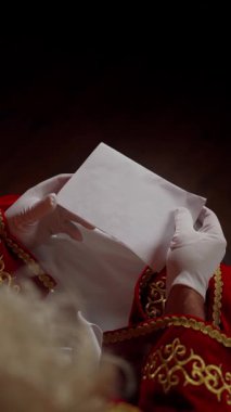 Kırmızı işlemeli takım elbiseli Aziz Nicholas bir zarf tutuyor. Dileklerle dolu bir Noel mektubunun okunduğu neşeli bir an..