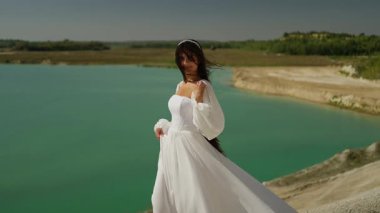 Turkuaz bir göl kenarında beyaz bir gelinlik içinde, kumlu sahilde çıplak ayakla yürüyen güzel bir gelin..