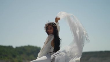 Beyaz elbiseli neşeli gelin peçesi güneşin altında çırpınıyor, mutlulukla dolu romantik bir düğün sahnesi..