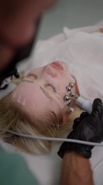 Kadın yüzünde yüz maskesi ile kaplanmış bir cihaz kullanarak kozmetik prosedürü, gençleştirme için spa kliniğinde cilt bakımı prosedürü.