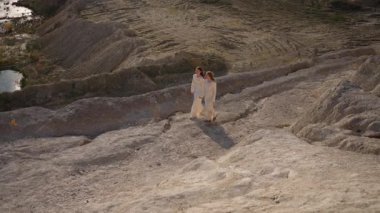 Beyaz elbiseli iki kadın dramatik kayalık arazide birlikte yürüyorlar..