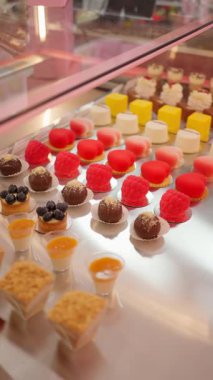 Pembe cam bir vitrin içinde sunulan renkli gurme çikolatalar ve tatlılardan oluşan bir karışım, geniş bir şekerleme seçeneği..