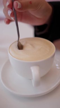 Bir fincan kapuçino ve kremalı köpük bir kaşık ile seramik bir fincanda beyaz bir masanın üzerinde..